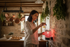 Middle Eastern woman pouring fragrance oil into red mosaic wall plug-in warmer in a French country kitchen